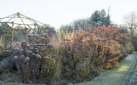 Frosted wooden rustic gazebo surrounded by decaying perennials and ornamental grasses in winter