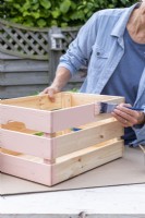 Woman painting wooden crate with pale orange pastel paint
