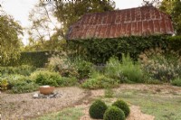 Gravel garden with bubbling water feature in front of barn with corrugated metal roof, at Terstan in September