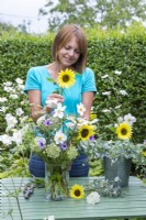 Woman placing Helianthus 'Buttercream' - Sunflower in a bouquet with Catananche, Ammi visnaga, white Anemone and Eucalyptus sprigs