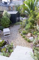 Small garden with black shed and curved gravel path running through the middle towards a seating area