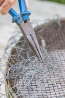 Woman using pliers to fix chicken wire to compost sieve