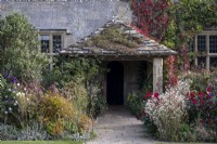 Informal overflowing autumnal borders with grasses and perennials, including Dahlia 'Dovegrove', Fennel, and Salvia. Old tiled porch at Gravetye Manor Gardens