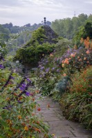 Paved path leading through misty autumnal borders in cottage-style garden, tiled summerhouse behind.  Dahlia 'David Howard', Tagetes 'Cinnabar' and Phlox 'Princess Sturdza' in the borders