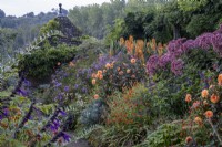 Paved path leading through misty autumnal borders in cottage-style garden, tiled summerhouse behind.  Dahlia 'David Howard', Tagetes 'Cinnabar' and Phlox 'Princess Sturdza' in the borders