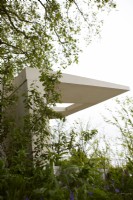 Memoria and GreenAcres Transcendence Garden. Designers: Gavin McWilliam and Andrew Wilson. Chelsea Flower Show 2023. Contemporary cantilevered pavilion against a stark white sky.