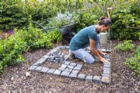 Woman placing Granite setts in a checkerboard pattern with a square outline