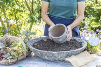 Woman placing pot in container of compost