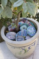 Painted stones made by children decorate a plant pot on a patio. May. 