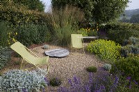 Drought tolerant garden filled with mediterranean plants.  Pea shingle seating area with yellow canvas deck chairs in The Jewel Garden -  Nepeta 'Six Hills Giant' - Catmint, Euphorbia seguieriana subsp. niciciana ,Echinops ritro 'Veitch's Blue',  Kniphofia 'Mango Popsicle'
 Stachys byzantina -  Lambs Ears,  grasses including  Stipa gigantea,   Buxus sempervirens balls - Box.  