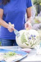 Woman using a wide brush to spread glue over the whole pumpkin as a glaze