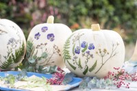 White pumpkins with pressed flowers and leaves on table with berries and eucalyptus sprigs