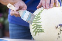 Woman brushing glue over fern to stick it to the pumpkin