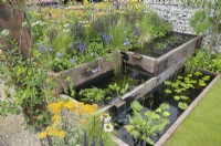 Urban garden with rectangular terraced ponds made from reclaimed materials linked with waterfall blades surrounded by wildlife-friendly perennials like Achillea, Echinacea, Salvia and Veronica.  Nuturing Nature in the City - RHS Hampton Court Palace Garden Festival 2023.  Designed by Caroline Clayton and Peter Clayton 