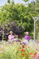 Two women sitting at table in garden near wooden arch