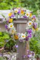 Wildflower wreath made of daisies,  wild onions, cow parsley, wheat  and  yellow ox-eye hanging from the table.