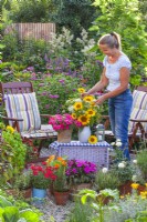 Woman making a floral arrangement with sunflowers on terrace with many containers planted with herbs and balcony flowers.