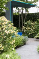 A curved path leads towards Azalea ponticum 'Daviesii' and a sheltered seating area on The National Brain Appeal's Rare Space Garden designed by Charlie Hawkes - RHS Chelsea Flower Show 2023