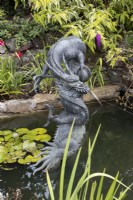 A large copper dragon sculpture, Chinese style, in a pond setting with a stream of water spraying from the mouth. Summer.