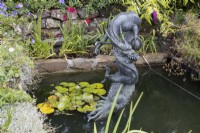 A large copper dragon sculpture, Chinese style, in a pond setting with a stream of water spraying from the mouth. Summer