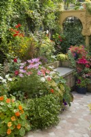 Small, paved courtyard garden styled with a Moroccan theme. Built in seat. Colourful bedding plants in containers with pelargoniums, nasturtiums, cosmos, bidens and begonias. July.