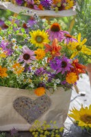 Bunch of harvested edible flowers in paper bag including sunflowers, monarda, coneflowers, hemerocallis, pot marigolds and chamomile.