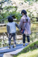 Japanese brother and sister holding hands and looking into pond. 