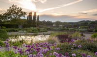 Sunrise view over the gravel garden towards Blagdon Lake - various varieties of alliums and mixed planting flower beds and small pond 