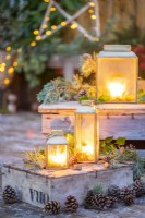 Lanterns on wooden crates with Pine sprigs and pinecones arranged around them