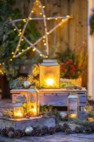 Lanterns on wooden crates with Pine sprigs, pinecones and baubles arranged around them