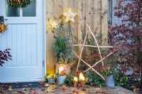 Candles in terracotta pots and one in a metal bucket with moss in front of Birch star, wicker pot containing Juniper, Cornus sticks and Eucalyptus sprigs with a trug of Ivy and wicker light up stars hanging on the wall above