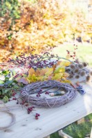 Twig wreath, Teasel seed heads, Beech and Portuguese laurel sprigs, Hawthorn, scissors, rope, secateurs, wire and scissors laid out on wooden surface