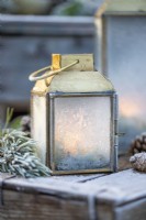 Small lantern frosted over with Pine sprigs and pinecones on wooden crates