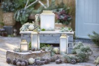 Small lanterns frosted over with Pine sprigs, pinecones and Baubles on wooden crates