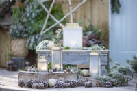Small lanterns frosted over with Pine sprigs, pinecones and baubles on wooden crates