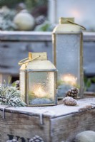 Small lanterns frosted over with Pine sprigs, pinecones and baubles on wooden crates