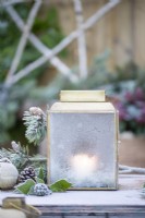 Lantern frosted over with Pine sprigs, pinecones and baubles on wooden crates