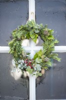 Wreath made of Yew, Ivy Hedera, Eucalyptus and Hawthorn berries hanging from door against frosted glass