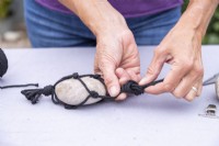 Woman tying all pieces of string into one knot above the pebble to hold it in place
