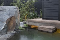 Timber frame wooden deck with steps leading down to a cold water plunge pool - a black painted fence with Malus domestica - Apple tree - large stone boulder - The Finnish Soul Garden RHS Chelsea Flower Show September 2021