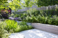 Built-in wooden bench seating with lush planting in raised bed in modern garden
