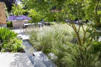 Lush planting in borders of modern garden with outdoor dining area