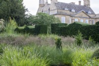 View across the grass borders towards clipped Taxus baccata hedges and the house at Bourton House Garden, Gloucestershire.