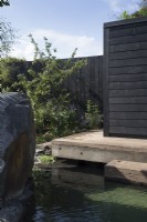 Timber frame wooden deck with steps leading down to a cold water plunge pool - a black painted fence with Malus domestica - Apple tree  - The Finnish Soul Garden RHS Chelsea Flower Show September 2021