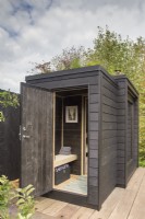Timber wooden deck with black painted wood sauna cabin with a living roof planted with wildflowers and herbs  - The Finnish Soul Garden RHS Chelsea Flower Show September 2021 