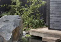 Timber frame wooden deck with steps leading down to a plunge pool - a black painted fence with Malus domestica - Apple tree underplanted with sedums - The Finnish Soul Garden RHS Chelsea Flower Show 2021