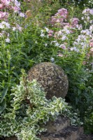 A round stone finial set against Saponaria officinalis.