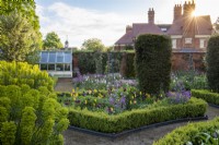 Daybreak in a Victorian walled garden. Set around a central arbour, a formal parterre is composed of box edged beds planted with tulips, honesty, euphorbia and a sea of leafy perennials. Yew columns add permanence.