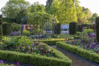 A Victorian walled garden has a central arbour, around which a formal arrangement of differently shaped, rope and box edged beds emanate: planted with tulips, honesty, euphorbia and a sea of leafy perennials. Yew columns add permanence.