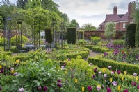 An arbour, hand forged by George James  and  Sons Blacksmiths, sits in a circular arrangement of box-edged beds planted with tulips, euphorbia, peonies and honesty. Yew columns add permanence.